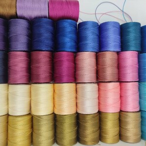 Peut inclure: Une collection de 36 bobines de fil de diff&eacute;rentes couleurs, dont le marron, le violet, le bleu, le rose, le beige, l'or et le bleu sarcelle. Les bobines sont dispos&eacute;es en rang&eacute;es et sont toutes de la m&ecirc;me taille.