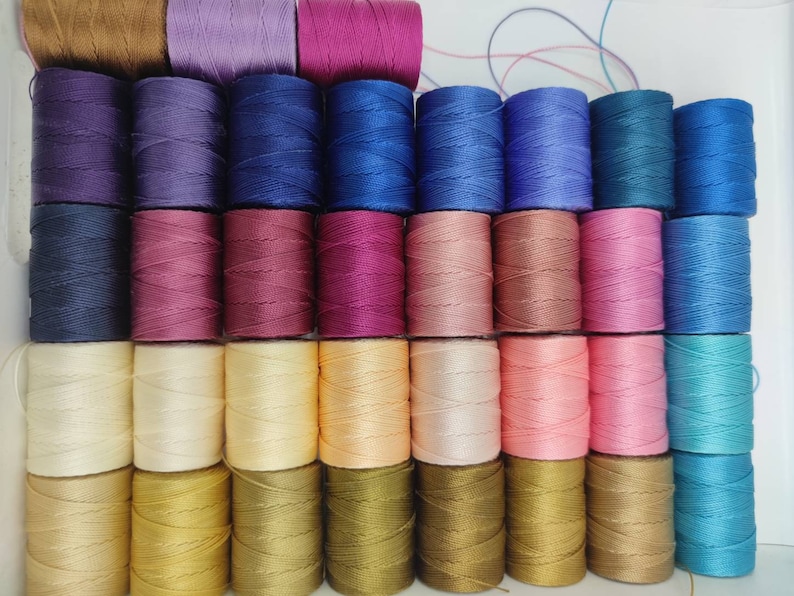 Peut inclure: Une collection de 36 bobines de fil de diff&eacute;rentes couleurs, dont le marron, le violet, le bleu, le rose, le beige, l'or et le bleu sarcelle. Les bobines sont dispos&eacute;es en rang&eacute;es et sont toutes de la m&ecirc;me taille.