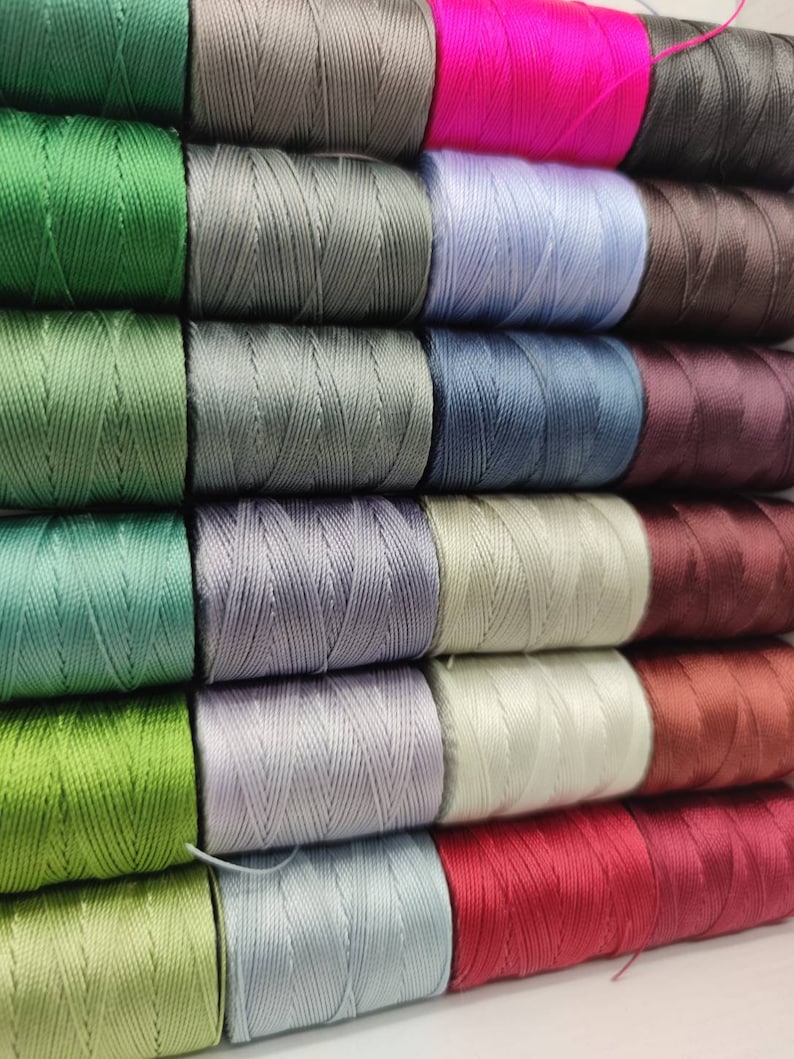 Peut inclure: Une collection de bobines de fil de diff&eacute;rentes couleurs, notamment vert, gris, bleu, rouge et marron. Les bobines sont dispos&eacute;es en rang&eacute;es, les couleurs alternant.