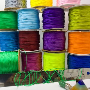 May include: Assortment of colorful spools of waxed cord, arranged in a pyramid shape. The cords are in various colors, including green, blue, purple, red, orange, yellow, and gray. A ruler is in the foreground, with a green cord wrapped around it.