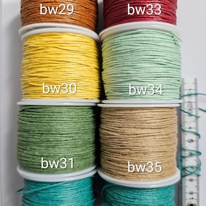 Puede incluir: Ocho carretes de cordón de colores dispuestos en dos columnas, etiquetados de bw29 a bw35. Los colores incluyen marrón, rojo, amarillo, verde claro, oliva, beige y cerceta. Una regla blanca está colocada verticalmente a la derecha en centímetros.