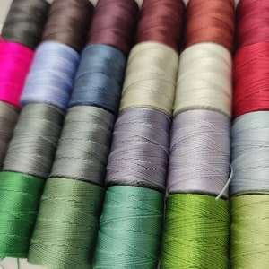 Peut inclure: Une collection de bobines de fil de diff&eacute;rentes couleurs, notamment rose, bleu, gris, vert et rouge. Les bobines sont dispos&eacute;es en rang&eacute;es et sont toutes de la m&ecirc;me taille.