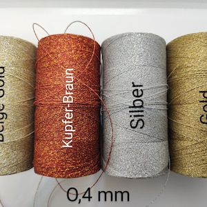 Może przedstawiać: Cztery szpulki metalicznej nici, każda w innym kolorze: beżowo-złoty, miedziano-brązowy, srebrny i złoty. Grubość nici wynosi 0,4 mm.