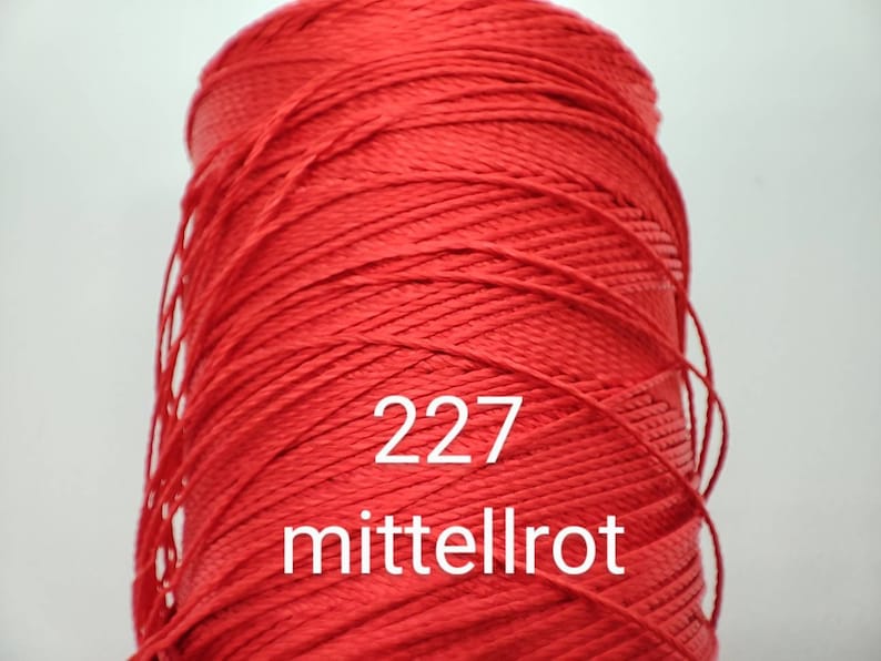 Puede incluir: Una bobina de hilo rojo con el n&uacute;mero 227 y la palabra "mittelrot" impresa en ella.