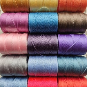 Pode incluir: Uma coleção de 15 carretéis de linha de bordado em várias cores, incluindo rosa, roxo, azul, vermelho, laranja, amarelo e marrom.
