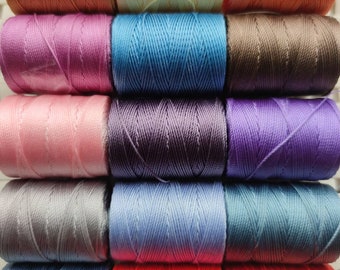 Könnte beinhalten: Eine Sammlung von 15 Spulen Stickgarn in verschiedenen Farben, darunter Rosa, Lila, Blau, Rot, Orange, Gelb und Braun.