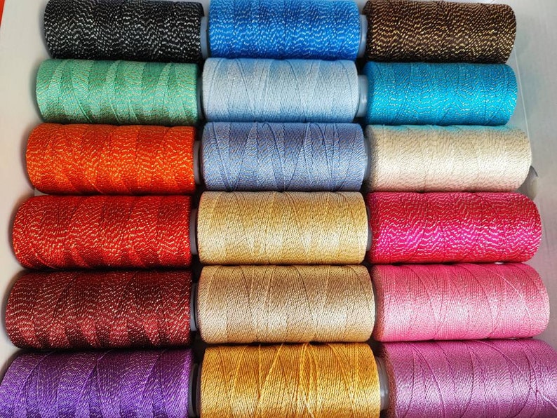 May include: A collection of 18 spools of thread in various colors, including black, blue, green, orange, red, gold, pink, purple, and white. Each spool has a metallic sheen.