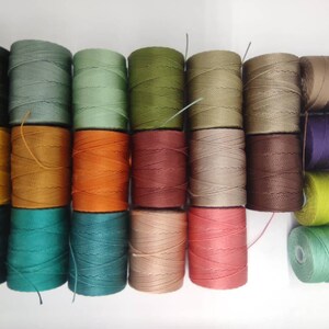 Peut inclure: Une collection de 20 bobines de fil de lin cir&eacute; de diff&eacute;rentes couleurs, notamment vert, marron, orange, rouge, beige et violet. Les bobines sont dispos&eacute;es en deux rang&eacute;es, la rang&eacute;e sup&eacute;rieure &eacute;tant l&eacute;g&egrave;rement d&eacute;cal&eacute;e par rapport &agrave; la rang&eacute;e inf&eacute;rieure.