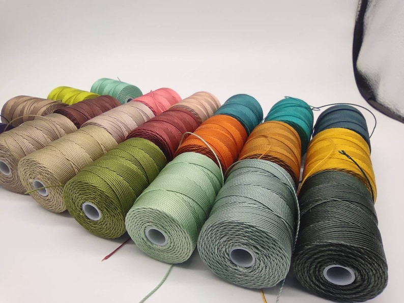 Peut inclure: Une collection de bobines de fil &agrave; broder color&eacute; dans diff&eacute;rentes nuances de vert, marron, orange, rouge et beige.