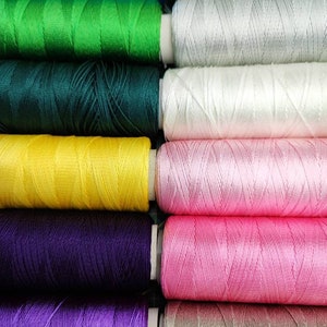 Puede incluir: Una colecci&oacute;n de carretes de hilo en varios colores, incluyendo azul, verde, amarillo, morado, rosa y blanco. Los carretes est&aacute;n dispuestos en una fila, con los colores alternando.