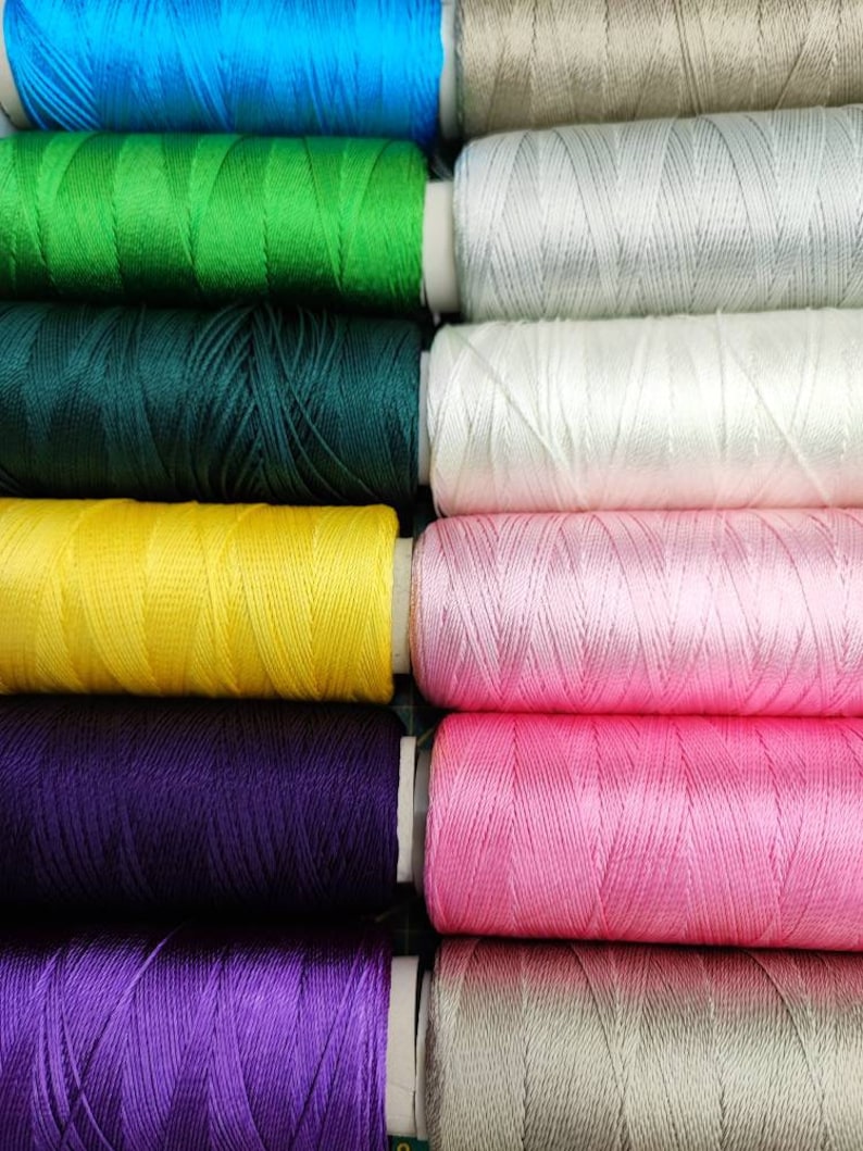 Puede incluir: Una colecci&oacute;n de carretes de hilo en varios colores, incluyendo azul, verde, amarillo, morado, rosa y blanco. Los carretes est&aacute;n dispuestos en una fila, con los colores alternando.