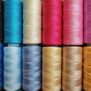 May include: A collection of 10 spools of thread in various colors, including brown, blue, beige, pink, purple, gold, and silver. The thread is wound tightly on each spool and has a shiny, metallic finish.