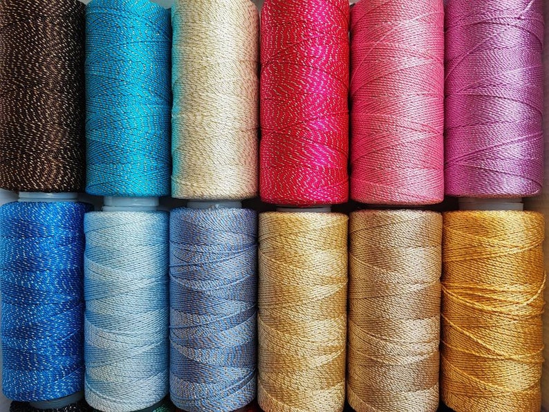 May include: A collection of 10 spools of thread in various colors, including brown, blue, beige, pink, purple, gold, and silver. The thread is wound tightly on each spool and has a shiny, metallic finish.