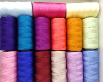 Pode incluir: Uma coleção de bobinas de linha coloridas em várias tonalidades, incluindo branco, rosa, roxo, azul, laranja e amarelo. As bobinas estão cuidadosamente dispostas, sugerindo um fornecimento de artesanato ou costura.