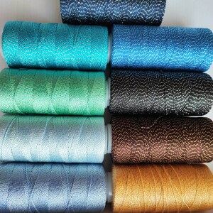 May include: A set of ten spools of thread with metallic accents. The spools are arranged in a stack, with the colors ranging from dark blue to gold.