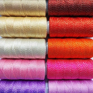 May include: Ten spools of metallic thread in various colors, including gold, red, orange, pink, and purple. The thread is wound around the spools and has a shiny, sparkly finish.