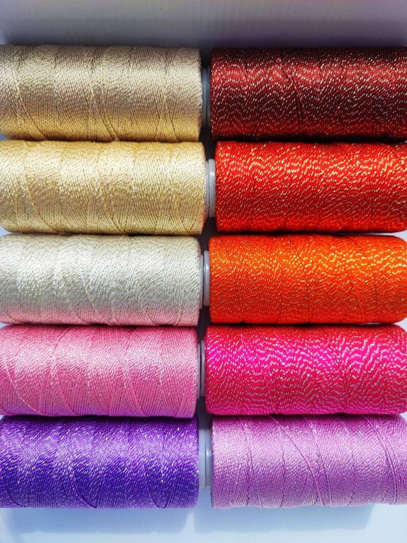 May include: Ten spools of metallic thread in various colors, including gold, red, orange, pink, and purple. The thread is wound around the spools and has a shiny, sparkly finish.