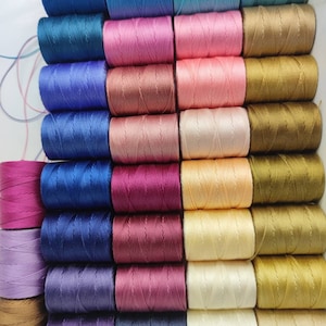 Peut inclure: Une collection de 24 bobines de fil de diff&eacute;rentes couleurs, notamment bleu, rose, marron, or, violet et rouge. Les bobines sont dispos&eacute;es en rang&eacute;es et en colonnes, et elles sont toutes de la m&ecirc;me taille.