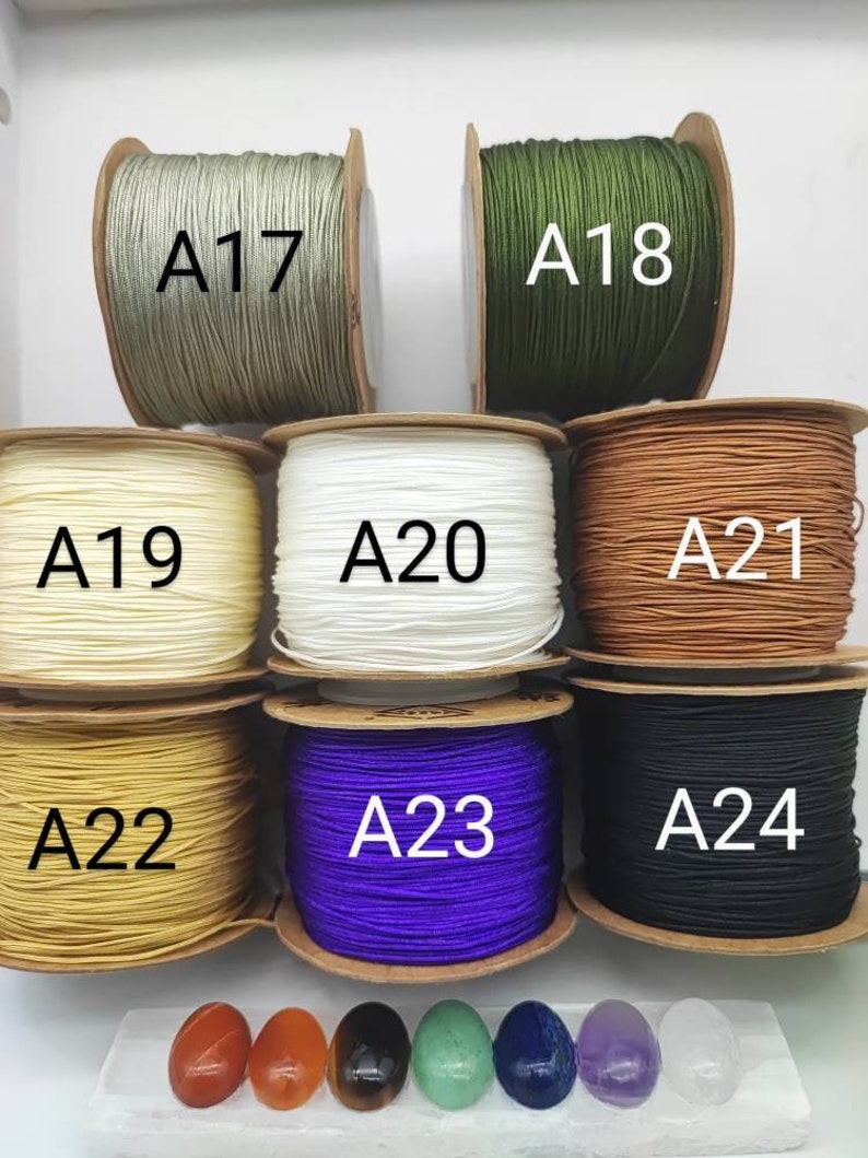 May include: Assortment of spools of waxed cord in various colors, including green, white, beige, yellow, purple, and black. Each spool is labeled with a letter and number, such as A17, A18, A19, A20, A21, A22, A23, and A24.  There are also seven small, smooth stones in various colors, including red, orange, brown, green, blue, purple, and white.