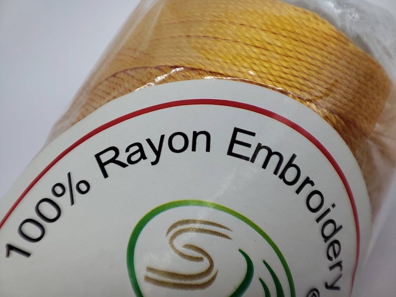 Puede incluir: Una bobina de hilo de bordar de ray&oacute;n 100% en color amarillo brillante. La etiqueta dice "100% Rayon Embroidery".