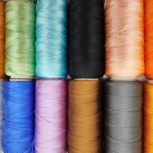Puede incluir: Una colecci&oacute;n de carretes de hilo en varios colores, incluyendo naranja, verde, azul, negro, marr&oacute;n, gris y amarillo.