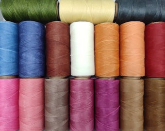 Op de afbeelding: Assortiment van 18 spoelen gewaxt garen in verschillende kleuren, waaronder groen, blauw, rood, bruin, roze en oranje. De spoelen zijn gerangschikt in drie rijen van zes.