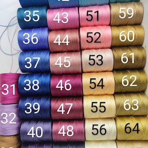 Peut inclure: Une collection de 65 bobines de fil &agrave; broder, dispos&eacute;es en rang&eacute;es de cinq. Les bobines sont num&eacute;rot&eacute;es de 31 &agrave; 65. Le fil est de diff&eacute;rentes couleurs, notamment bleu, rose, rouge, violet et or.