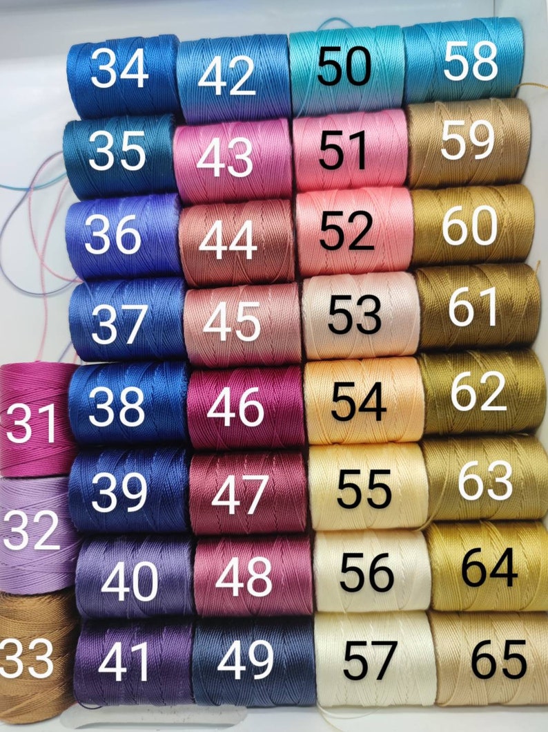 Peut inclure: Une collection de 65 bobines de fil &agrave; broder, dispos&eacute;es en rang&eacute;es de cinq. Les bobines sont num&eacute;rot&eacute;es de 31 &agrave; 65. Le fil est de diff&eacute;rentes couleurs, notamment bleu, rose, rouge, violet et or.