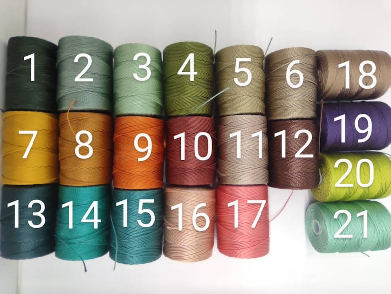 Peut inclure: Vingt et un bobines de fil de diff&eacute;rentes couleurs, num&eacute;rot&eacute;es de 1 &agrave; 21. Les bobines sont dispos&eacute;es en trois rang&eacute;es.