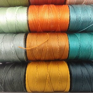 Peut inclure: Bobines de fil de diff&eacute;rentes nuances de vert, orange et marron. Le fil est enroul&eacute; serr&eacute; sur les bobines, cr&eacute;ant un aspect textur&eacute;.