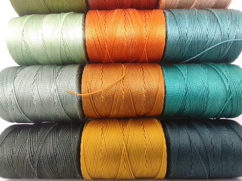 Peut inclure: Bobines de fil de diff&eacute;rentes nuances de vert, orange et marron. Le fil est enroul&eacute; serr&eacute; sur les bobines, cr&eacute;ant un aspect textur&eacute;.