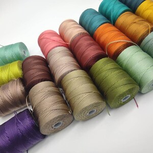 Peut inclure: Assortiment de bobines de fil de diff&eacute;rentes couleurs, y compris des nuances de vert, marron, beige, violet, rouge, orange et jaune.
