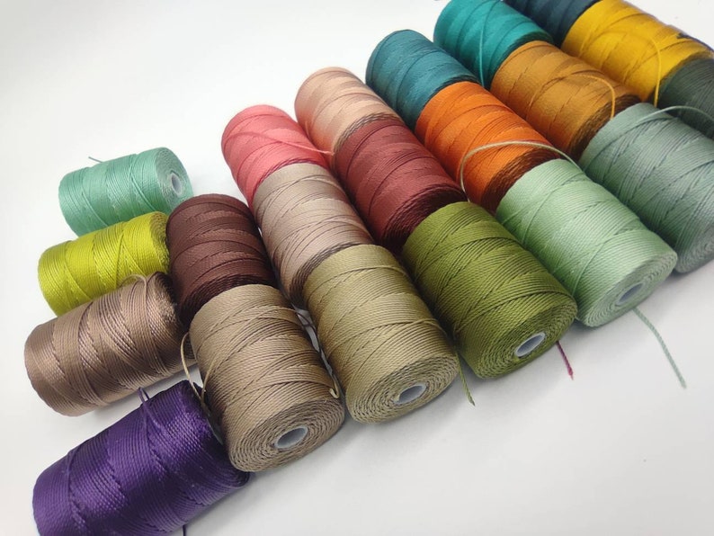 Peut inclure: Assortiment de bobines de fil de diff&eacute;rentes couleurs, y compris des nuances de vert, marron, beige, violet, rouge, orange et jaune.