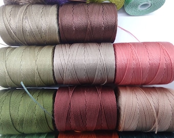 Könnte beinhalten: Nahaufnahme von Garnrollen in verschiedenen Farben, darunter Grün, Braun, Beige und Rosa. Das Garn ist fest auf den Rollen aufgewickelt und erzeugt eine strukturierte Oberfläche.