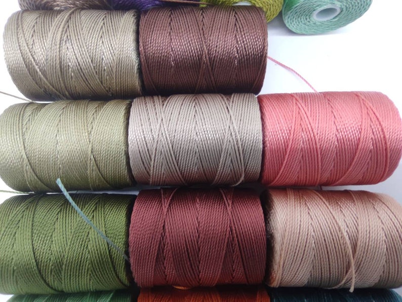 Peut inclure: Gros plan sur des bobines de fil de diff&eacute;rentes couleurs, notamment vert, marron, beige et rose. Le fil est enroul&eacute; serr&eacute; sur les bobines, cr&eacute;ant un aspect textur&eacute;.