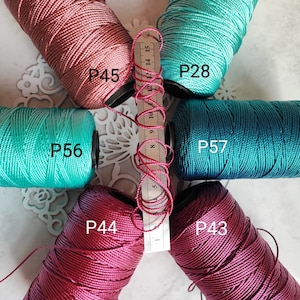 Può includere: Sei bobine di filo di diversi colori, tra cui turchese, bordeaux e rosa. Le bobine sono etichettate con i numeri P28, P43, P44, P45, P56 e P57.