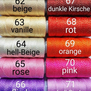 May include: Close-up of ten spools of embroidery floss in various colors, including beige, vanilla, rose, pink, and purple. Each spool is labeled with a number and a color name in German.
