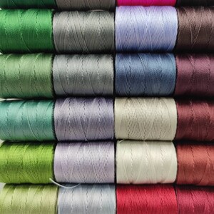 Peut inclure: Une collection de 18 bobines de fil de diff&eacute;rentes couleurs, notamment le vert, le gris, le bleu, le violet, le marron et le rouge. Les bobines sont dispos&eacute;es en trois rang&eacute;es de six.