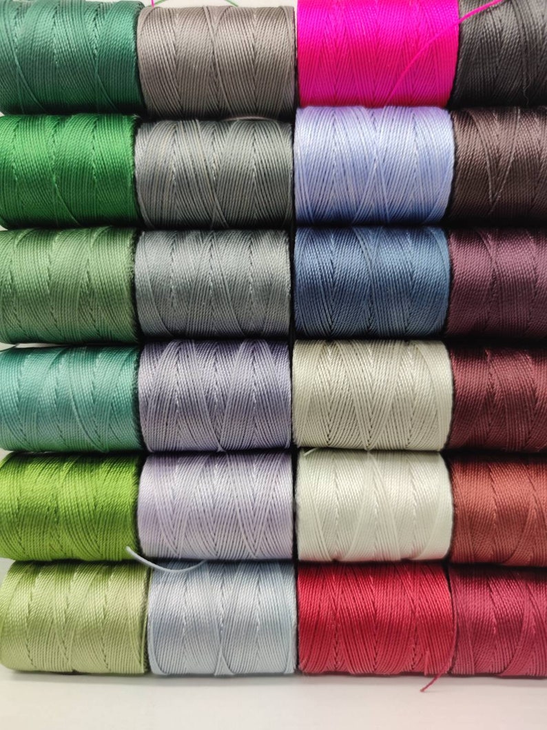 Peut inclure: Une collection de 18 bobines de fil de diff&eacute;rentes couleurs, notamment le vert, le gris, le bleu, le violet, le marron et le rouge. Les bobines sont dispos&eacute;es en trois rang&eacute;es de six.