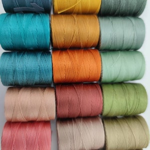 Peut inclure: Une collection de 12 bobines de fil &agrave; broder de diff&eacute;rentes couleurs, notamment turquoise, orange, marron et vert.