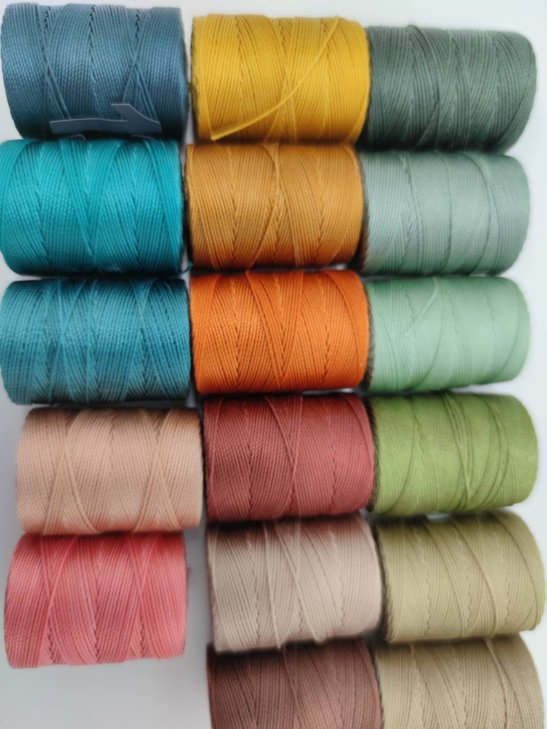 Peut inclure: Une collection de 12 bobines de fil &agrave; broder de diff&eacute;rentes couleurs, notamment turquoise, orange, marron et vert.