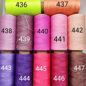 Könnte beinhalten: Neun Spulen mit gewachstem Garn in verschiedenen Farben, darunter Neongrün, Orange, Pink, Lila und Braun. Die Spulen sind mit den Nummern 436 bis 447 beschriftet.