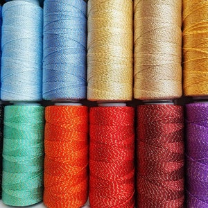 May include: Assortment of 12 spools of thread with metallic accents in various colors, including black, teal, orange, red, burgundy, and purple.