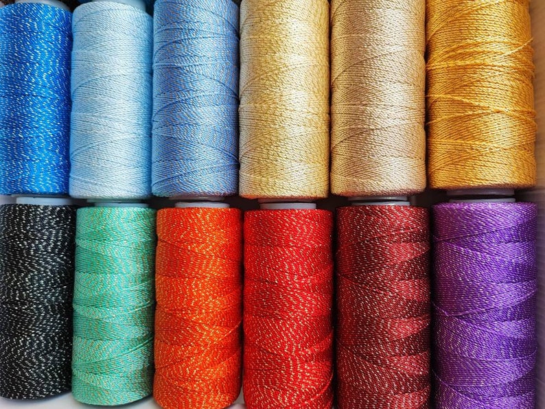 May include: Assortment of 12 spools of thread with metallic accents in various colors, including black, teal, orange, red, burgundy, and purple.