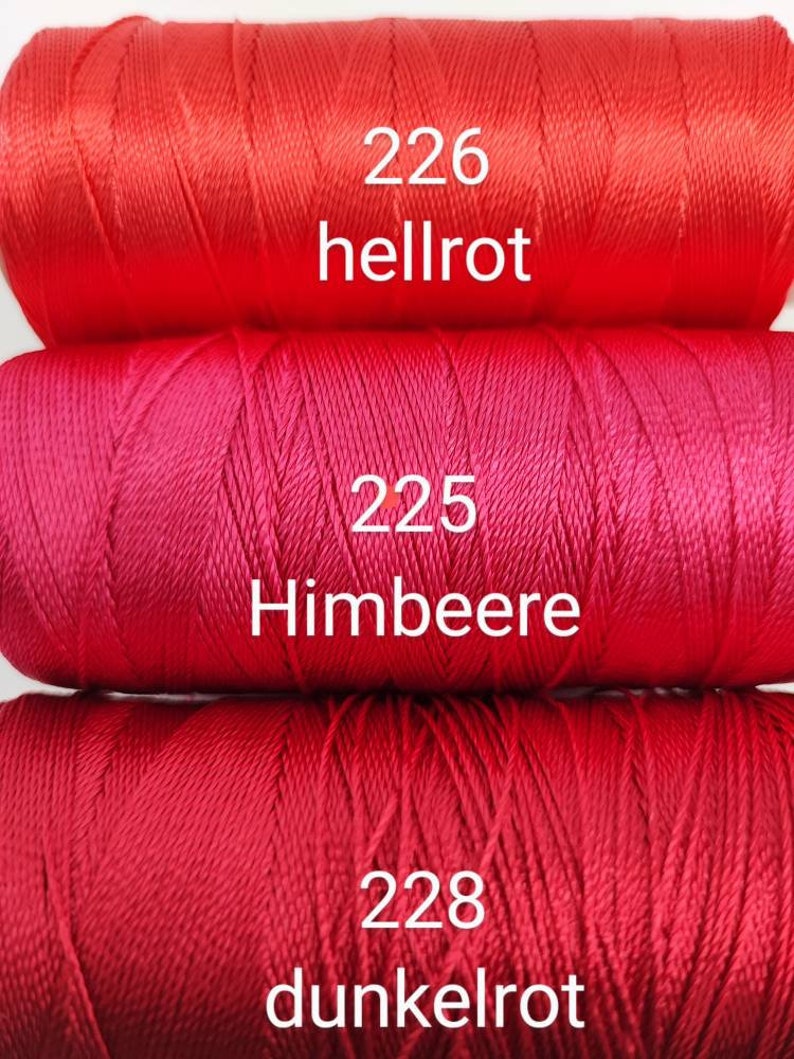 Puede incluir: Tres carretes de hilo de bordar rojo. El carrete superior est&aacute; etiquetado como "226 hellrot", el carrete del medio est&aacute; etiquetado como "225 Himbeere" y el carrete inferior est&aacute; etiquetado como "228 dunkelrot".