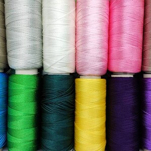 Puede incluir: Una colecci&oacute;n de carretes de hilo en varios colores, incluyendo beige, gris, blanco, rosa, azul, verde, verde oscuro, amarillo, morado y lavanda.