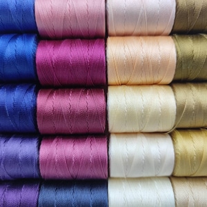 Peut inclure: Une collection de bobines de fil de diff&eacute;rentes nuances de bleu, violet, rose, beige et or.
