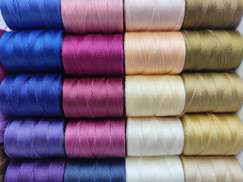Peut inclure: Une collection de bobines de fil de diff&eacute;rentes nuances de bleu, violet, rose, beige et or.