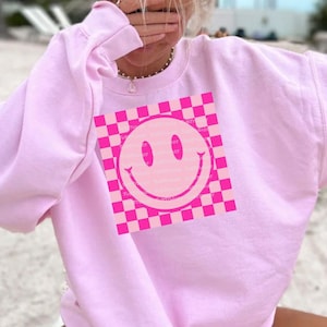 May include: Pink sweatshirt with a pink and white checkered smiley face graphic.