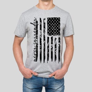 Puede incluir: Una camiseta gris con un diseño de bandera estadounidense desgastada en blanco y negro y el texto "never surrender" impreso en el lado izquierdo de la bandera.